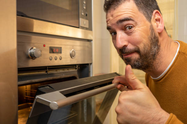 istock Nice bearded man in an orange sweater making the Ok gesture with his thumb when opening the oven int the kitchen at home 1305145806