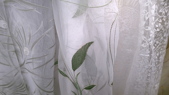 Samples of different types of white luxury tulle. Embroidery of green leaves. Delicate fabric background. Textiles and Apparel industry development. Craft. Idea for home decor and interior.