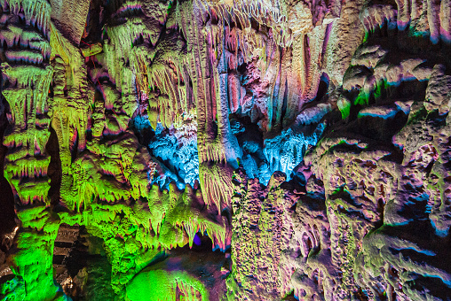 Guilin, China - May 10, 2010: Green, purple, and blue lights produce show on dripping Stalactite rocks in Reed Flute Cave.
