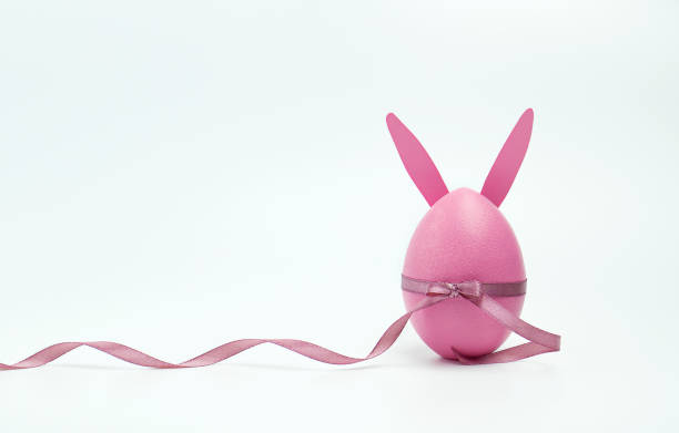 istock Easter pink egg with bunny ears, decorated with a satin ribbon on a white background. Happy Easter concept. Copy space 1305147902