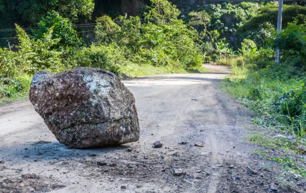 Large boulder sitting in middle of a dirt country road blocking traffic.