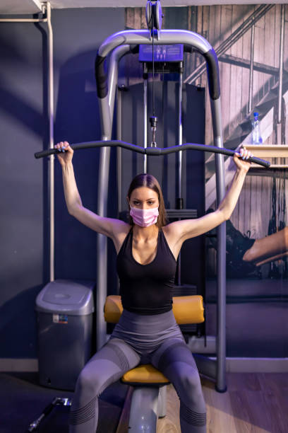 istock Young fitness woman wearing face mask  execute exercise with exercise-machine Cable Crossover in gym 1305150923