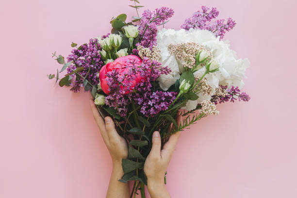 istock Hands holding modern bouquet on bright pink background flat lay. Peony, lilac, eucalyptus, hydrangea 1305154654
