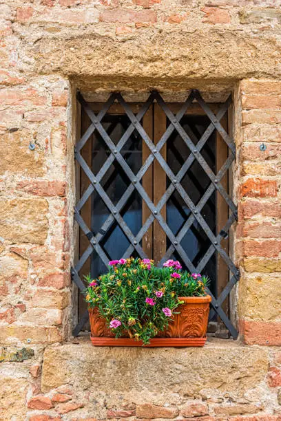 Monticchiello, Italy town village city in Tuscany closeup of pink flower pots decorations on summer day with stone wall architecture and small window