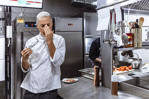 Worried chef at industrial kitchen in restaurant standing with eyes closed.