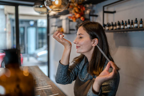 Young Perfumer preparing perfume while sitting at table in her own store stock photo