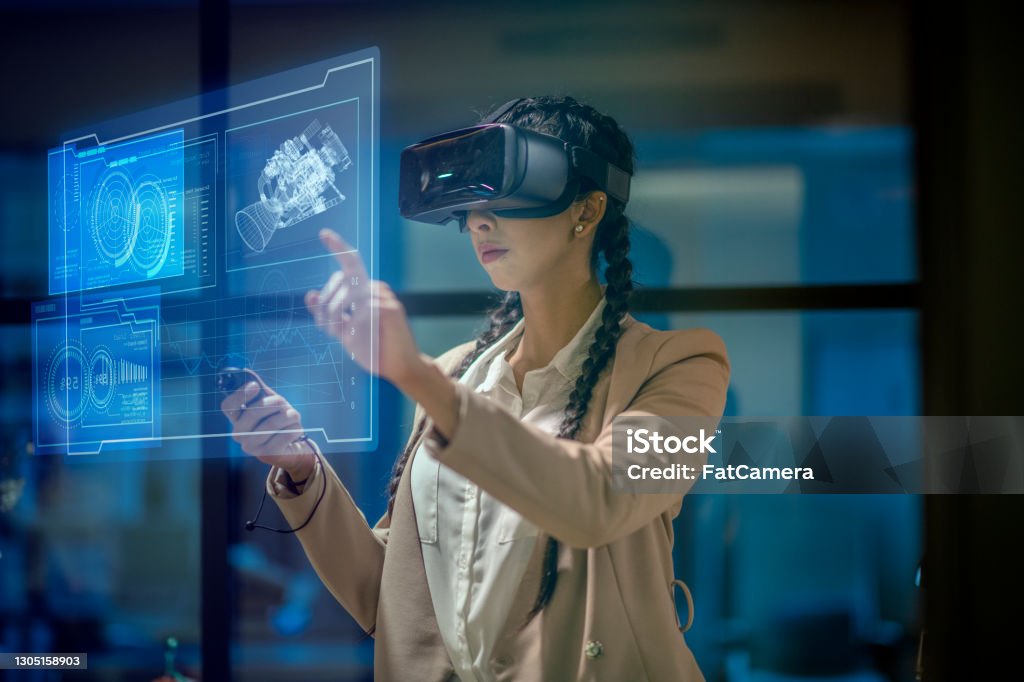 Woman wearing a VR headset at work Female engineer wearing a virtual reality headset at work to explore an upcoming mechanical engineering project. She uses her hands to manipulate and explore the finer details. Virtual Reality Simulator Stock Photo