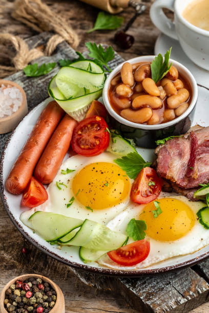 Traditional English breakfast with fried eggs, bacon, beans, coffee and sausage, Restaurant menu, dieting, cookbook recipe. vertical image