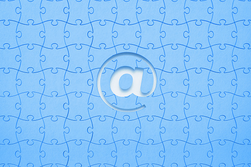 Blue jigsaw puzzle pieces forming a cut out at symbol on white background. Horizontal composition with copy space. Social media and email marketing concept.