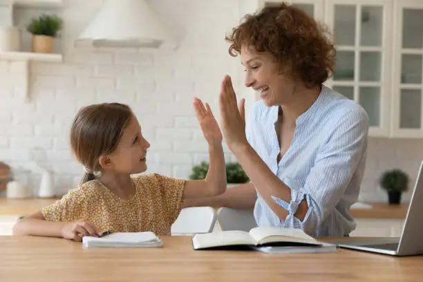 Well done dear. Excited mother give high five to small daughter praise child for reaching success in homework. Joyful female tutor greet schoolgirl for giving correct answer solving hard math problem