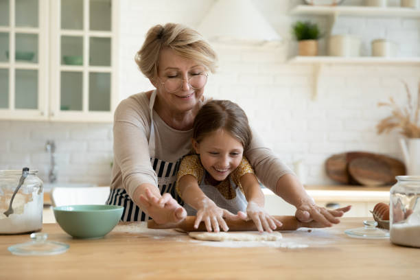 高齢のおばあちゃんは、ピンで生地を転がす小さな孫を含みます - grandmother domestic life cooking domestic kitchen ストックフォトと画像