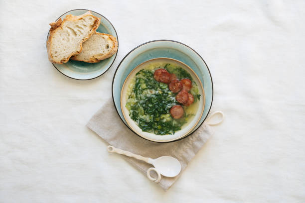 Caldo Verde Soup with greens and chopped chorizo on the top in ceramic bowl over ceramic plate on cotton bag with ceramic spoon. Pieces of bread on the plate. Top View stock photo