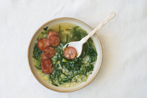 Caldo Verde Soup with greens and chopped chorizo on the top in ceramic bowl with ceramic spoon. Top View stock photo