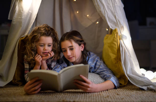 istock Sisters indoors at home, using reading book in pajamas. Lockdown concept. 1305176749