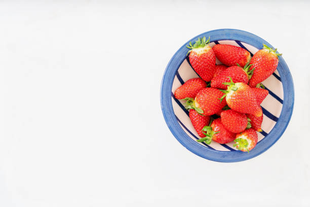 Fresh juicy strawberries in ceramic bowl isolated over white background. Top view. Copy space