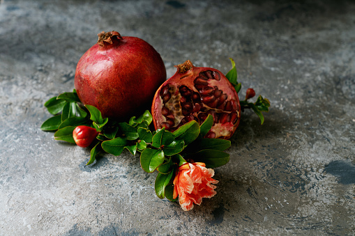Pomegranate fruits, whole and half, decorated with pomegranate flowering branch over rustic background. Close up. Selective focus