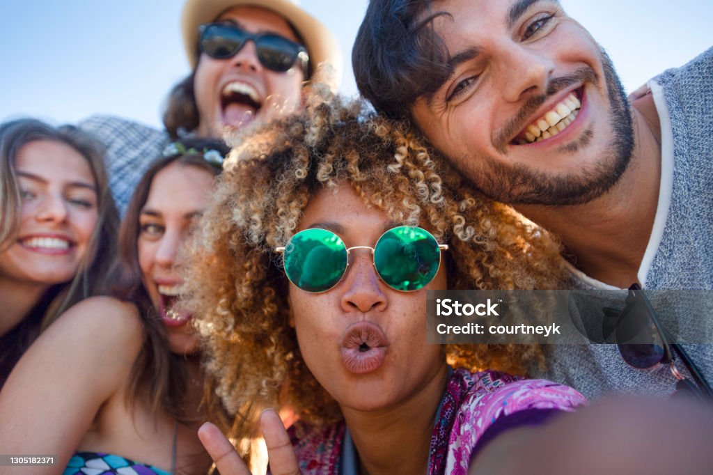 Group of friends having fun taking a selfie. Group of friends having fun taking a selfie. They are all looking at the camera and smiling and laughing. Some are making funny faces. Background is blue sky on a sunny day. Friendship Stock Photo
