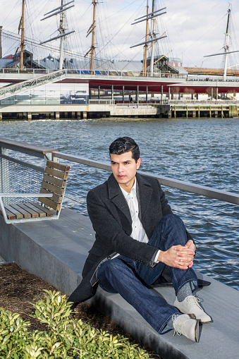 A young businessman is sitting by a river and into deeply thinking.