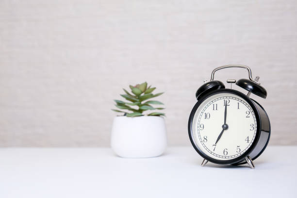 istock An alarm clock showing 7 o'clock standing on a white table with copy space, everyday shedule and morning wake up concept 1305184193