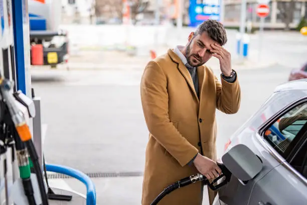 Worried man refueling his car's tank at the gas station in the city.