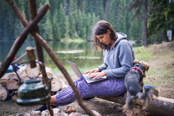 istock Young beautiful woman sitting next to campfire and using her portable computer. 1305189920