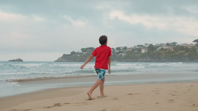 Relaxed boy enjoying summer at beach. Carefree guy skipping at coastline.