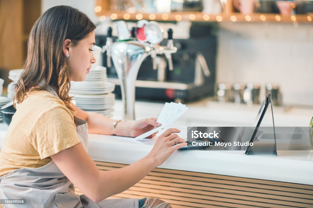 How much did we make? Shot of a young woman using a digital tablet and calculator while going through paperwork in a cafe Making Money Stock Photo