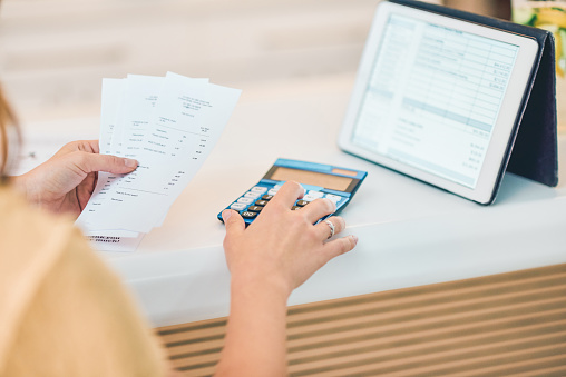 Shot of a woman using a digital tablet and calculator while going through paperwork in a cafe