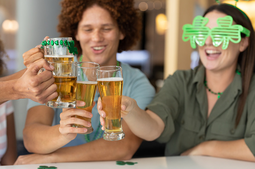 Diverse group of happy friends celebrating st patrick's day making toast with glasses of beer at bar. fun during celebration of the irish patron saint's day.
