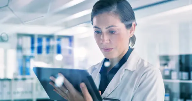 Shot of a young woman using a digital tablet while going through notes on a glass screen in a lab