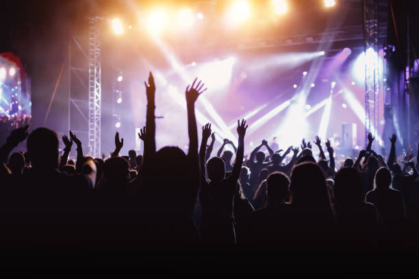 Rock concert, cheering crowd in front of bright colorful stage lights Rock concert, cheering crowd in front of bright colorful stage lights, Hands up with pleasure from the show popular music concert stock pictures, royalty-free photos & images