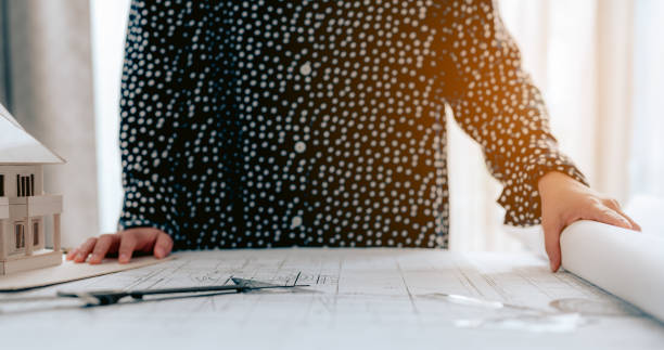 istock Close-up,female architect viewing Blueprint, customer factory construction project in the evening.Architect, Engineer, Architecture, Design, Planning, Occupation concept. 1305212821