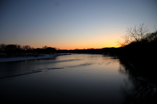 Wide angle shot of a snow lined rocky river bend on the Cedar River, Iowa at sunset.