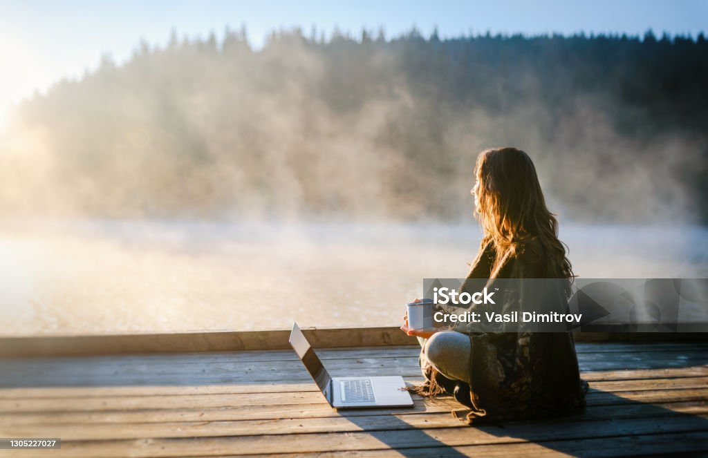 Woman Relaxing In Nature And Using Technology Young woman working on  laptop in the nature . Leisure activities / Remote working concept. Telecommuting Stock Photo