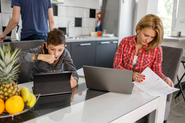 istock Boy having breakfast over digital tablet when sitting by his mother working with paperwork and a laptop 1305227039