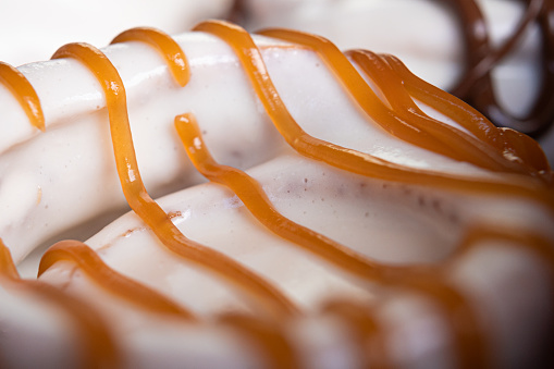 Delicious homemade cinnamon roll dipped in white glaze garnished with caramel in close up.