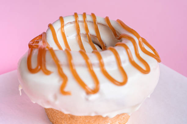 istock Delicious freshly baked cinnamon roll covered with white cream garnished with caramel on a pink background. 1305233533