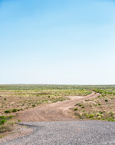 At the remote end of a deserted gravel asphalt highway, an empty winding dirt road stretches off into the distant prairie wilderness of the San Rafael Desert in the western USA state of Utah.