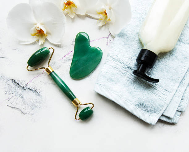 istock Face massage jade roller with cosmetic product on white marble background 1305243944