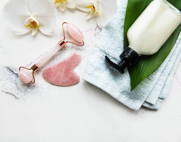 istock Face massage jade roller with cosmetic product on white marble background 1305243950