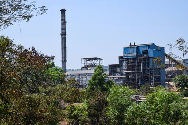 Stock photo of a factory located middle of Indian village or countryside surrounded by green trees in a sunny day at kolhapur city Maharashtra India, blue color factory with chimney. Stock photo of a factory located middle of Indian village or countryside surrounded by green trees in a sunny day at kolhapur city Maharashtra India, blue color factory with chimney. kolhapur stock pictures, royalty-free photos & images