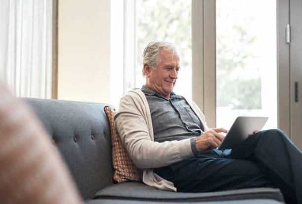 Familiarising myself with modern day technology Cropped shot of a senior man sitting alone on his sofa at home and using a tablet familiarising stock pictures, royalty-free photos & images