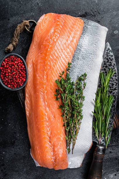 istock Fresh raw salmon fillet fish on cutting board with knife. Black background. Top view 1305249998