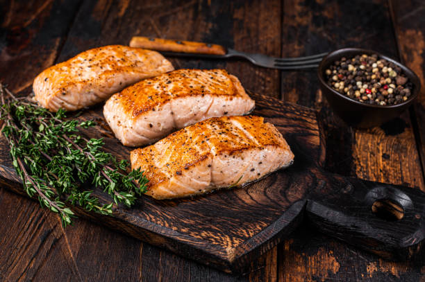 filetes de filete de salmón frito en una tabla de madera con tomillo. fondo de madera oscura. vista superior - alimentos cocinados fotografías e imágenes de stock