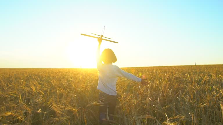 Happy little boy child running with toy airplane in wheat field at sunset. Kid playing with airplane in summer nature outdoors, Little pilot dreaming of flight travel vacation happy family big dream