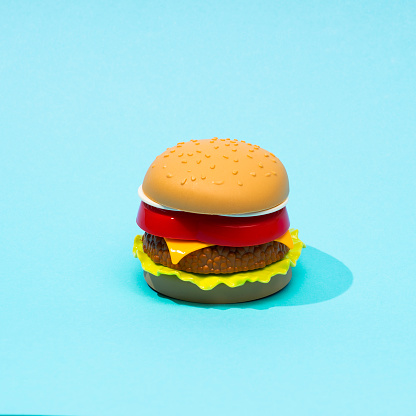 Plastic childrens toy burger with salad, tomato, meat with on pastel blue background. Concept of harmful artificial food. Unhealthy. Not organic. Not useful. Top view. Food pattern.
