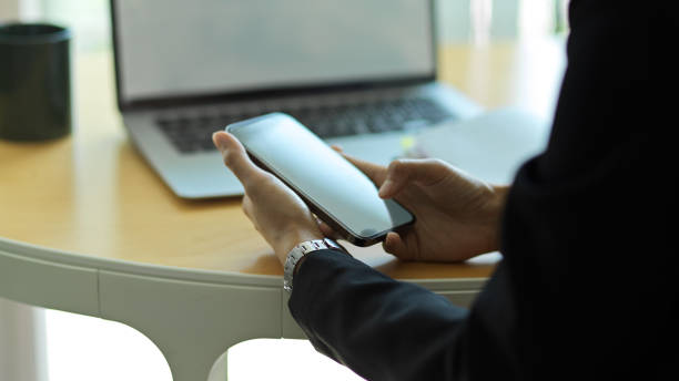 istock Businessman using smartphone while sitting at workspace with laptop in background 1305256738