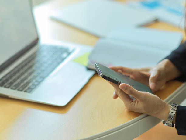 istock Businessman using smartphone in his hands on workspace with laptop and supplies 1305256740