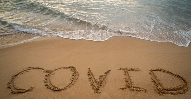 istock Handwriting COVID on sand and foam wave on beach. Coronavirus concept. 1305256751