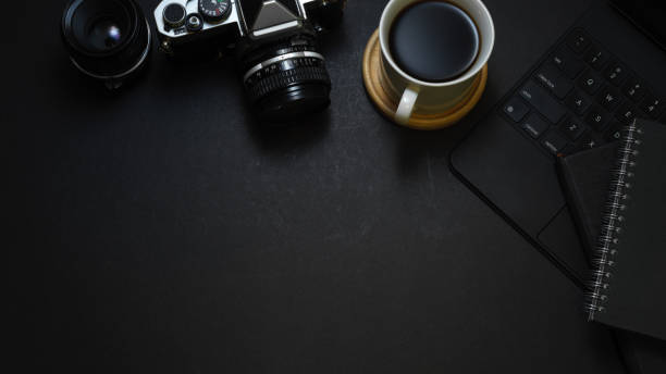 istock Dark creative workspace with coffee cup, camera, supplies and copy space, mock up scene 1305257291
